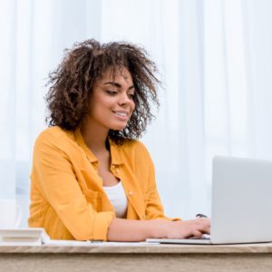 Photo of a woman with curly hair smiling while on her laptop.