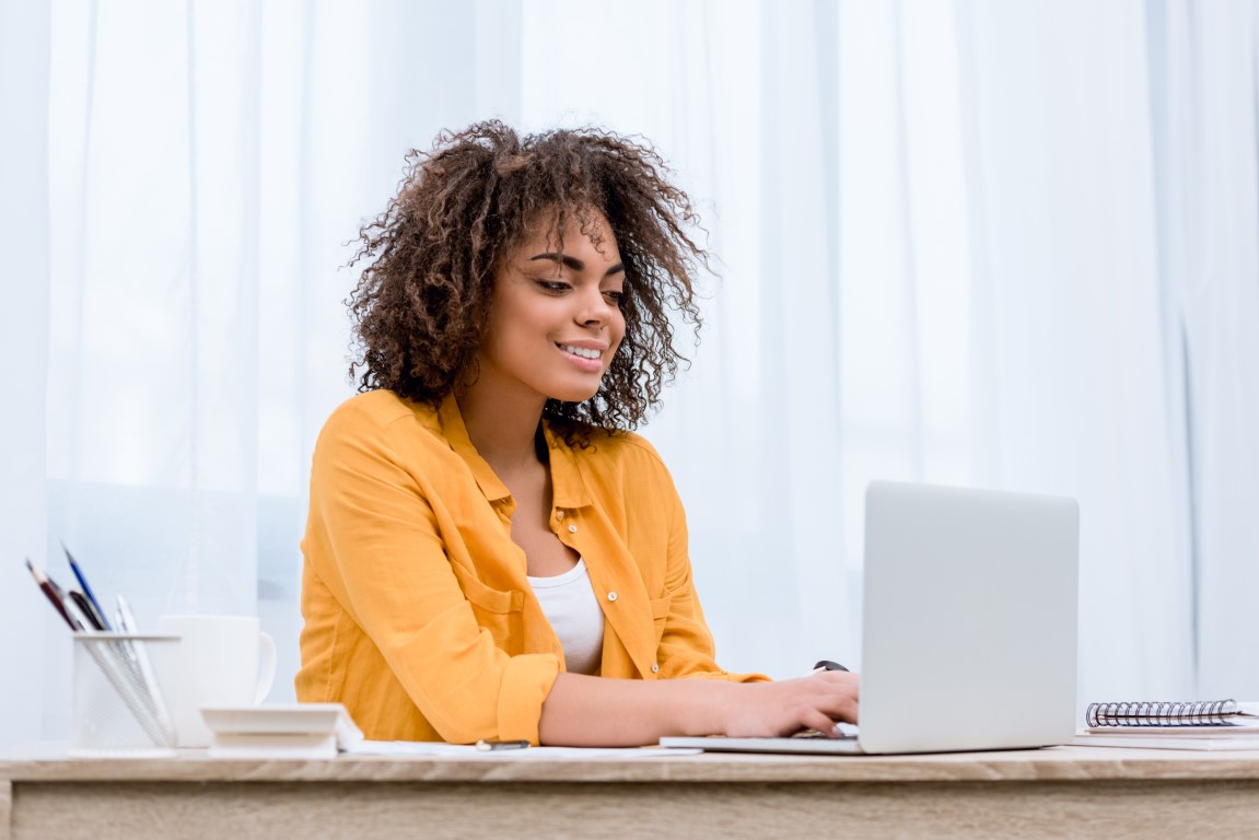 Photo of a woman with curly hair smiling while on her laptop.