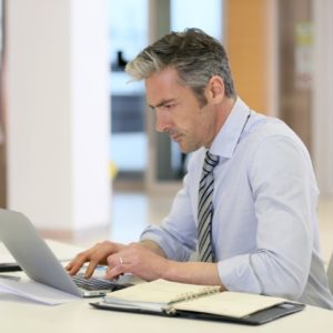 Man in dress shirt working on a laptop.