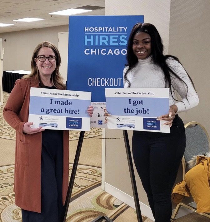 Women employer and job seeker taking a picture together in front of a Hospitality Hires Chicago sign.