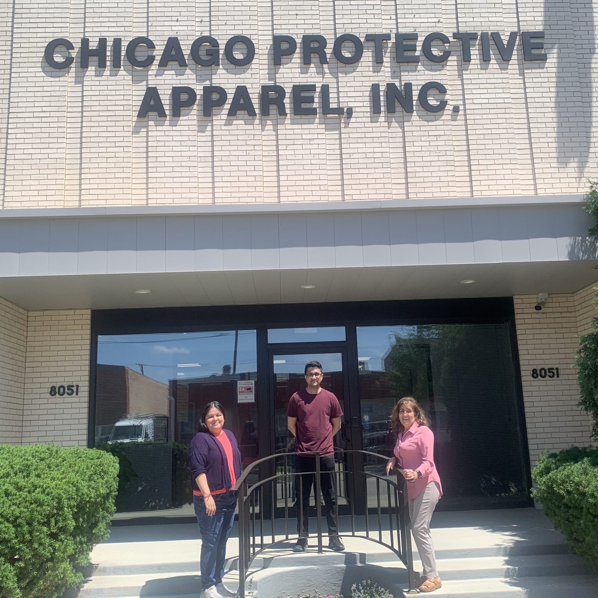 A man and two women standing at the top of the stairs of a brick building with a sign in big letters, 