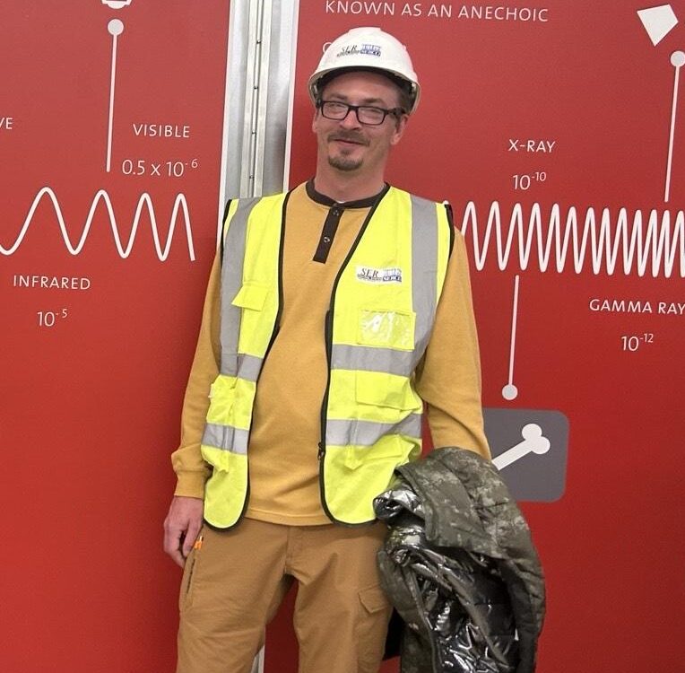 A photo of a man wearing a white hard hat and a high visibility yellow vest.