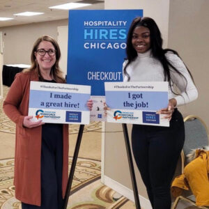 Women employer and job seeker taking a picture together in front of a Hospitality Hires Chicago sign.
